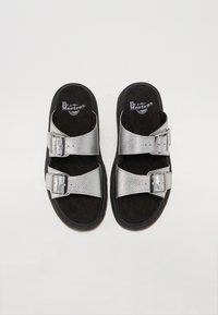 Sandale din faux piele argintie cu două catarame ajustabile, insole din suede negru și un finisaj texturat pe curele. Talpă din cauciuc negru.