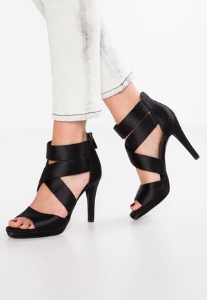 Zwarte satijnen hoge hakken sandalen met kruislings gespen en een open teen ontwerp. Voorzien van een taps toelopende hak en een ritssluiting aan de achterkant.