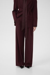 Burgundy tailored suit with a wide-leg pant and a matching blazer. Features a long satin tie and smooth fabric texture.