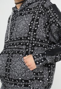 Sudadera con capucha en blanco y negro con un patrón intrincado de diseños paisley, un bolsillo frontal y una capucha con cordón, con una textura suave.
