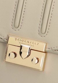 Borsa a mano in pelle grigia chiara con chiusura in metallo dorato dotata di logo inciso e accessori decorativi. Texture liscia e linee pulite.
