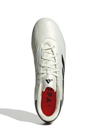 Zapato de fútbol sintético blanco con acentos en negro y interior rojo. Presenta un diseño con cordones, superficie texturizada y un cuello acolchado para mayor comodidad.