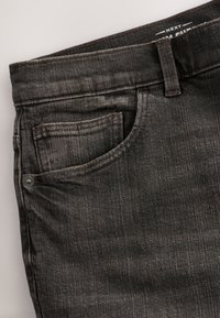 Jean en denim gris foncé montrant la poche avant, la petite poche, la passoire pour ceinture et la taille avec une étiquette de marque partiellement visible à l'intérieur de la ceinture.