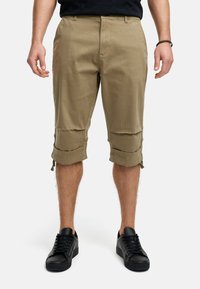 Shorts cargo beiges avec des ourlets roulés ajustables, fabriqués en tissu léger. Portés avec des baskets noires, dotées d'un système de laçage.