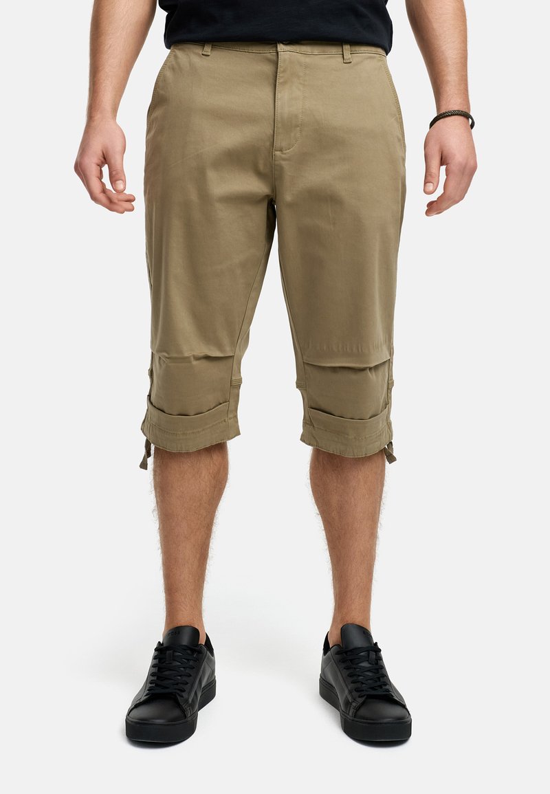 Beige cargoshorts met verstelbare opgerolde mouwen, gemaakt van lichtgewicht stof. Gepaard met zwarte sneakers, met vetersluiting.