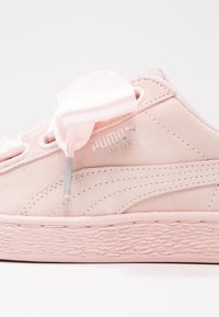 Tenisky Puma Suede v světlé růžové nubukové kůži s texturovanou mezipodešví, saténovými stahovacími šňůrkami a malým stříbrným logem na straně.
