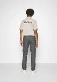 Beige short-sleeve polo shirt with black logo text on the back, paired with dark textured trousers and white sneakers.