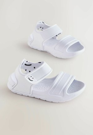 Sandali bianchi con cinturini regolabili, suola testurizzata e stampa di un volto sorridente sulla fodera interna. Materiale in gomma e design open-toe.