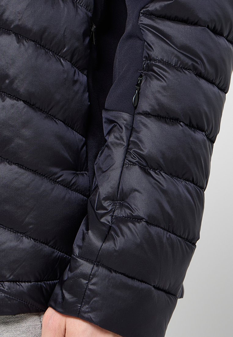 Dunkelblauer Pufferjacke mit gesteppten Abschnitten, glatter Textur und einer Reißverschlusstasche an der Seite zur Aufbewahrung.