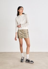 Pull beige à manches longues associé à une jupe mini à motif serpent. Le mannequin porte des baskets noires et grises avec des chaussettes blanches.