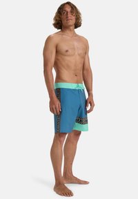 Bañadores de hombre en azul y verde menta, con una banda estampada en el lateral, cinturilla con cordón y material ligero.