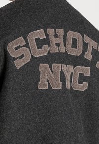 Dark grey wool-blend jacket featuring beige chenille "SCHOTT NYC" lettering, with a textured finish and a classic crew neckline.
