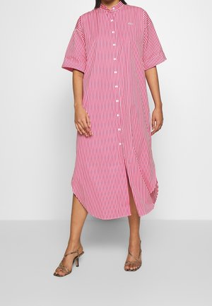Femme portant une robe midi boutonnée à rayures verticales rouges et blanches avec des manches courtes et des sandales à talons imprimé serpent.