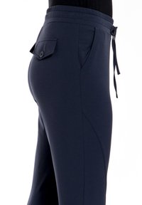 Marineblauwe sportbroek met een gladde textuur, elastische tailleband en koorddetails. Voorzien van een achterzak met een knoopsluiting.