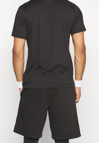 Camiseta atlética negra de manga corta y pantalones cortos, fabricados con un tejido suave. La camiseta tiene mangas cortas, y los pantalones cortos son de longitud hasta la rodilla con un corte holgado.