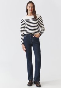 Maglione a righe in crema e blu navy, abbinato a jeans blu scuro. Il maglione ha un collo a coste; i jeans presentano una vestibilità classica con cuciture sottili.