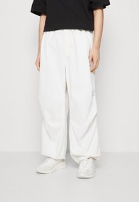 Pantalones de pierna ancha blancos, hechos de algodón con una textura suave, que presentan una costura frontal y bolsillos, combinados con zapatillas de color claro.