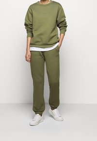 Olivegrön bomulls sweatshirt och matchande sweatpants med ribbade manschetter, bärs med en vit lager-på-lager skjorta. Vita sneakers fulländar looken.
