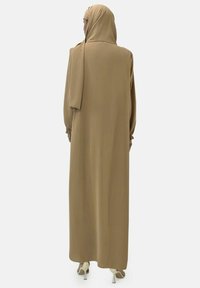 Lange, loszittende jurk van beige stof met lange mouwen en een bijpassende hoofddoek. Voorzien van geplooide manchetten en een eenvoudig ontwerp.