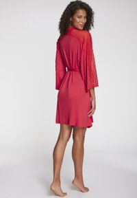 Crveni kimono haljina sa čipkastim detaljima na rukavima, vezana u struku, s mekim, glatkim teksturom i dizajnom do koljena.