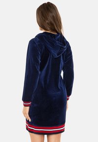 Abito felpa in velluto blu navy con maniche lunghe, avente polsi e orlo a strisce rosse e bianche, vista posteriore che mostra il cappuccio.