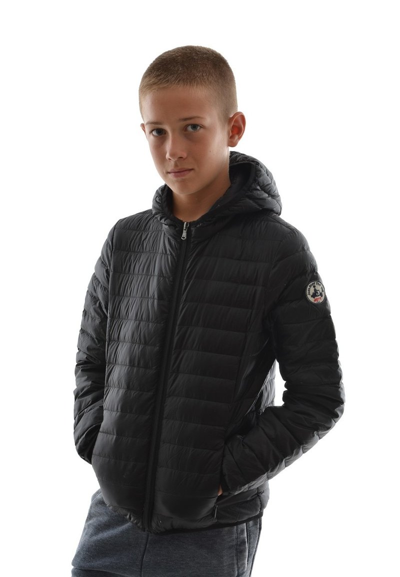Doudoune noire avec une capuche, présentant une texture matelassée, une fermeture éclair à l'avant et un patch logo sur la manche gauche. Portée avec un pantalon de survêtement gris.