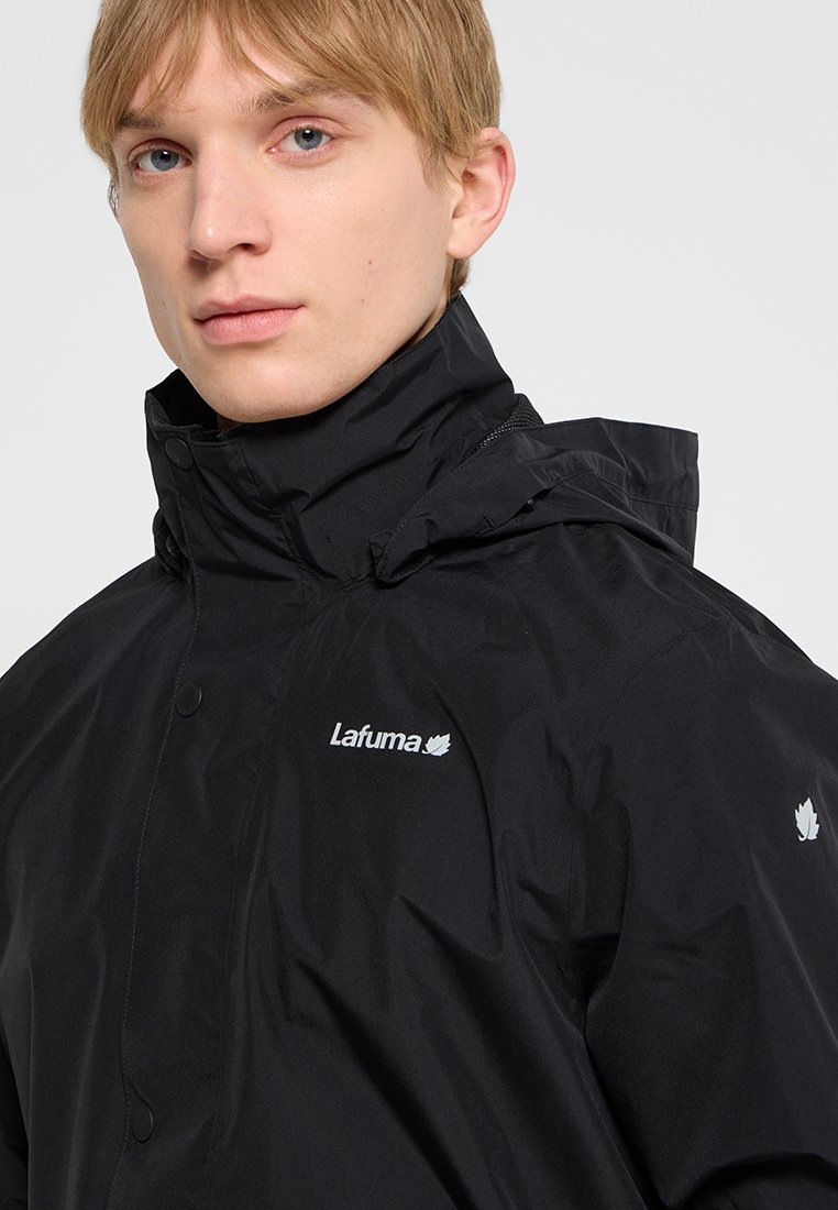 Jongere met kort blond haar, gekleed in een zwart Lafuma-jack met hoge kraag en zichtbaar merklogo op de borst en mouw.