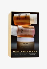 Zestaw produktów OUAI w pudełku zawierający trzy pojemniki: dwie plastikowe butelki z złotym gradientem (szampon detoksykujący, żel pod prysznic) oraz biały słoik (peeling do ciała).