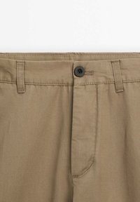 Pantalon de couleur kaki avec fermeture à bouton noir, passants de ceinture et coutures visibles sur la ceinture et la zone de la braguette.