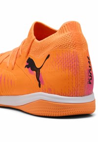 Lys orange atletisk sko med struktureret stof, kontrasterende sort logo og gradient pink accenter på siderne. Hvid mellemsål.