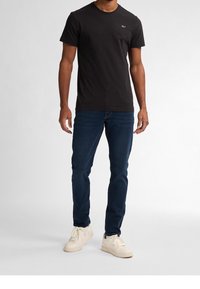 Černé bavlněné tričko s kulatým výstřihem a decentním logem na hrudi, v kombinaci s tmavě modrými džíny a krémovými teniskami.