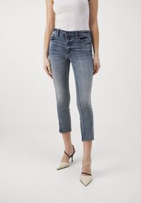 Tmavě modré zkrácené džíny s mírným vyblednutím, designem s pěti kapsami a prošitým lemem, kombinované s béžovými lodičkami s špičatou špičkou.