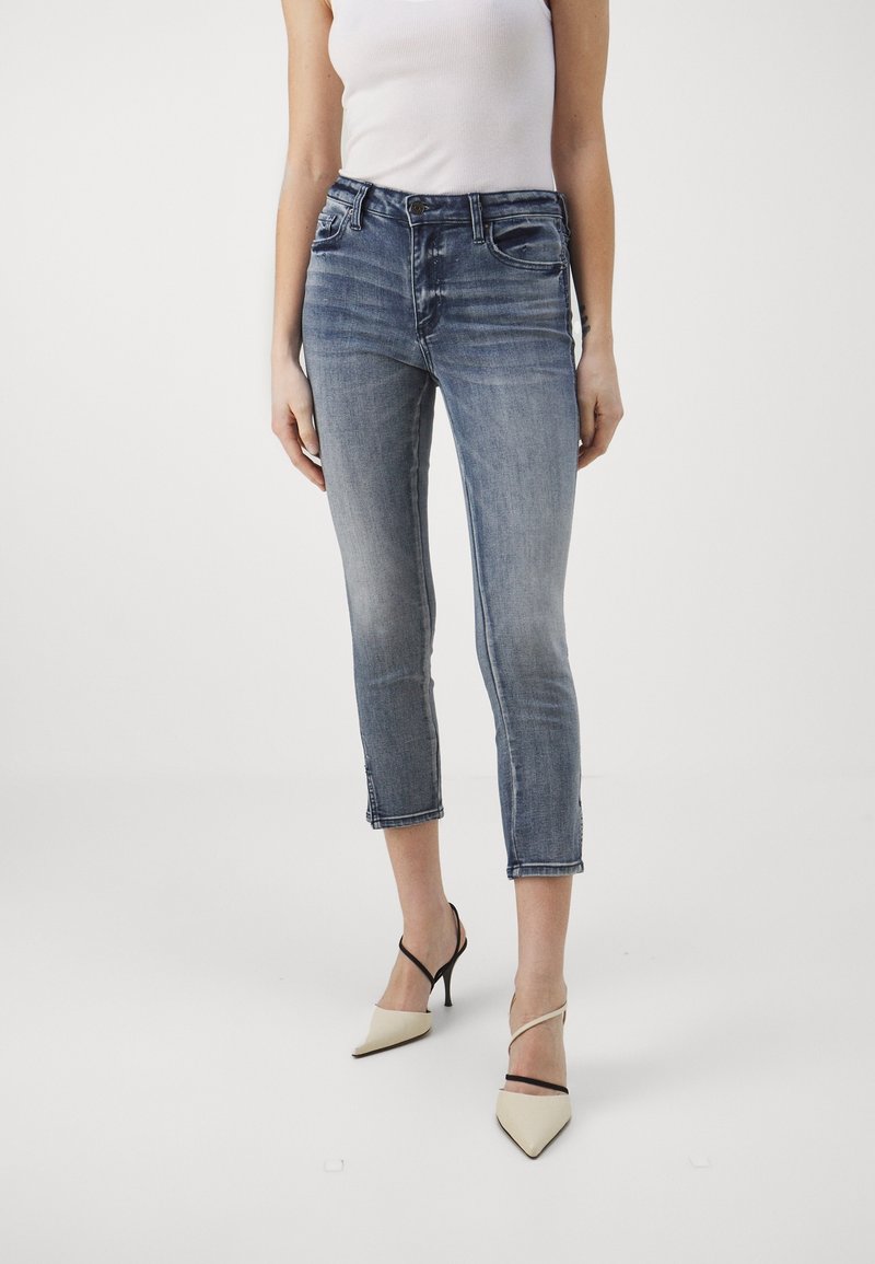 Tmavě modré zkrácené džíny s mírným vyblednutím, designem s pěti kapsami a prošitým lemem, kombinované s béžovými lodičkami s špičatou špičkou.