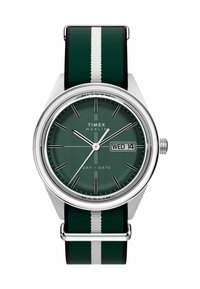 Timex Marlin sat s zelenim brojčanikom, srebrnim detaljima i crno-zelenom prugastom tekstilnom narukvicom. Ima prikaz dana/datuma i minimalistički dizajn.
