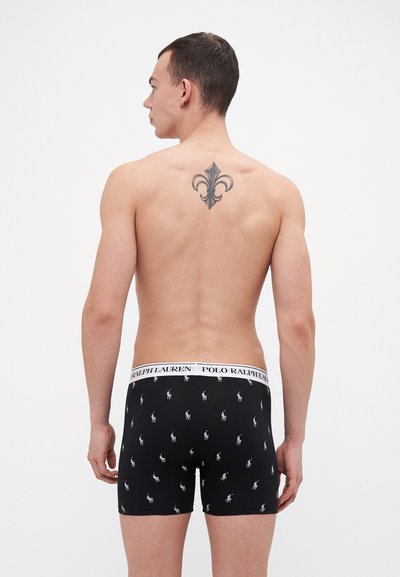 Zwarte boxershorts met een witte Polo Ralph Lauren tailleband; voorzien van een herhaald patroon met een klein paardenlogo. Het model heeft een zichtbare tatoeage op zijn rug.