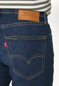 Dark blue denim jeans with a brown leather label at the waist, yellow stitching, and classic back pocket design featuring a red Levi's tag.