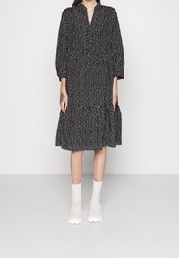 Schwarzes und weißes gemustertes Kleid mit V-Ausschnitt, dreiviertel Ärmeln, einem gestuften Saum und einer lockeren Passform. Kombiniert mit weißen Ankle Boots.