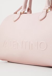 Bolsa de mão em pele rosa texturizada com o logo em relevo "VALENTINO", duas alças superiores e fundo robusto. Textura suave com um brilho subtil.