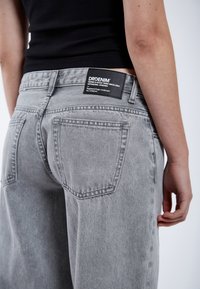 Grijze denimjeans met een relaxte pasvorm, met achterzakken, zichtbare naden en een zwart merketiket op de tailleband.