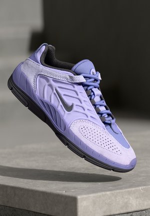 Paars sportieve schoen met textuurmateriaal, mesh accenten, perforaties, platte zwarte zool en grijze veters, voorzien van een zilveren logo aan de zijkant.