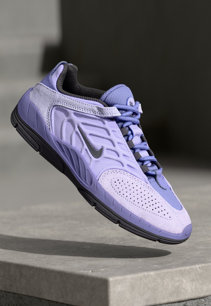 Scarpa sportiva viola con materiale testurizzato, accenti in rete, perforazioni, suola nera piatta e lacci grigi, che presenta un logo argento sul lato.