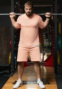 Abbigliamento sportivo rosa chiaro composto da una maglietta a maniche corte e pantaloni corti, entrambi con una vestibilità comoda. Scarpe da ginnastica bianche completano il look.