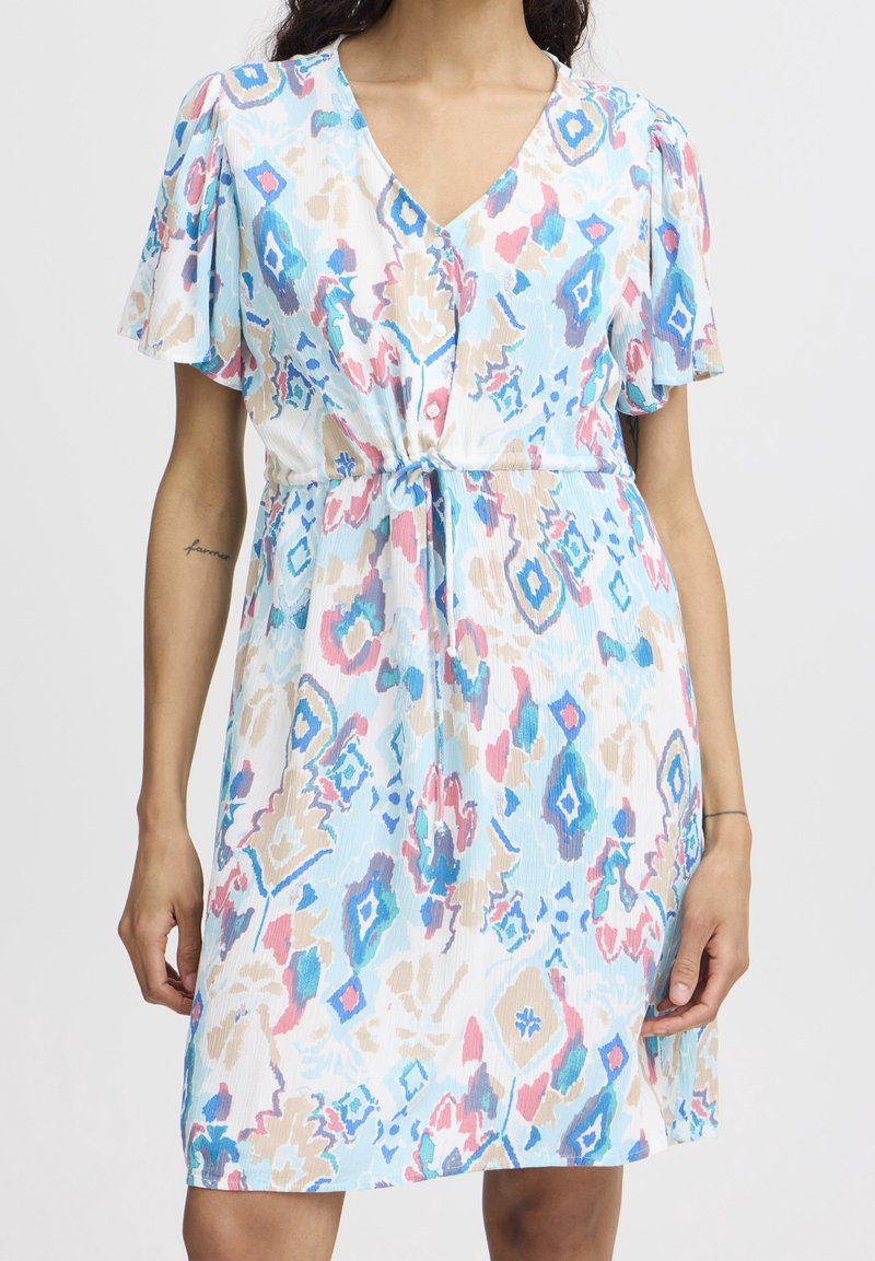 Robe à manches courtes avec col en V, taille nouée et motif floral abstrait bleu pastel, rose, beige et blanc, portée par une personne debout.