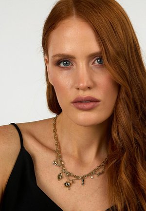 Goldfarbene Charm-Halskette mit mehreren Anhängern, darunter Blätter und Sonnenbrillen, an einem Modell, das ein schwarzes Top mit Spaghettiträgern trägt.