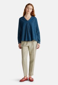 Haut en denim avec un col en V et des plis, associé à un pantalon beige clair à motifs et des ballerines tissées rouges. Style simple, coupe décontractée et design fluide.
