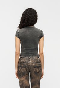 Εφαρμοστό t-shirt κοντομάνικο από ξεθωριασμένο μαύρο τζιν με στρογγυλή λαιμόκοψη· συνδυασμένο με καφέ τζιν ψηλόμεσο, ελαφρώς φθαρμένο, με τσέπες στο πίσω μέρος.