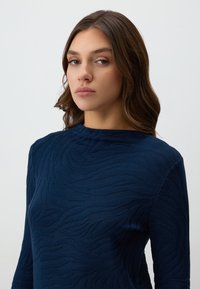 Top blu navy con un motivo ondulato testurizzato, scollatura rotonda e maniche lunghe, realizzato in un tessuto morbido e leggero.