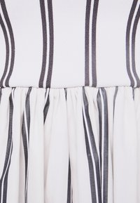 Tissu blanc avec des rayures verticales gris foncé, froncé à la couture où deux matériaux de textures différentes se rencontrent.