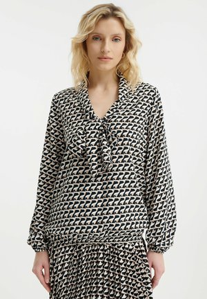 Blusa maniche lunghe in tessuto nero e crema con un motivo geometrico, colletto con fiocco e polsini arricciati con dettagli plissettati sull'orlo.