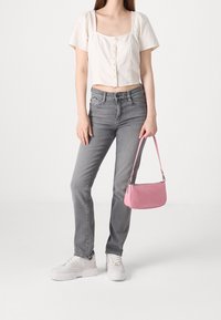 Top corto blanco de manga corta con botones, jeans gris de pierna recta y un bolso de textura rosa. El calzado son zapatillas blancas con suelas elevadas.